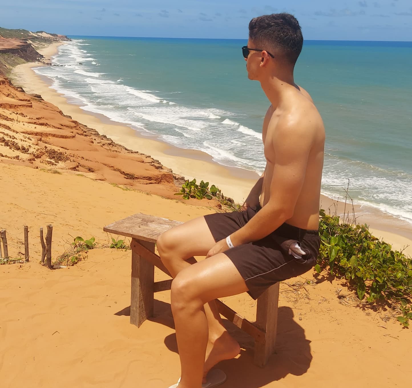 Pessoa sentada num banco de madeira em cima de uma falésia olhando o mar